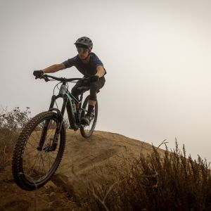 Mountain biker on enduro bike riding over boulder
