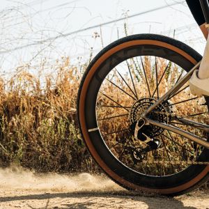A gravel bike with CADEX GXR tires creates a small dust trail as it rolls down a dirt road at speed.