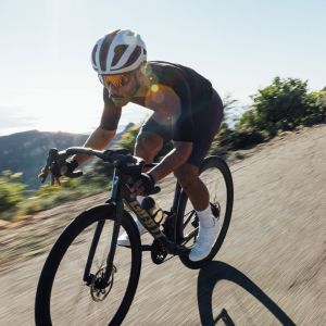 A cyclist descends a sunny mountain road in the drops of their Giant road bike wearing a Giant Rev Pro Helmet.