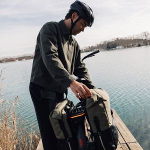 A cyclist uses the panier on their Giant AnyTour E+ electric city bike that's stopped on a dock by a lake.