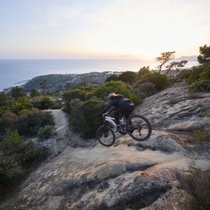 A mountain biker on a Giant Stance E+ trail bike descends a technical rocky drop.