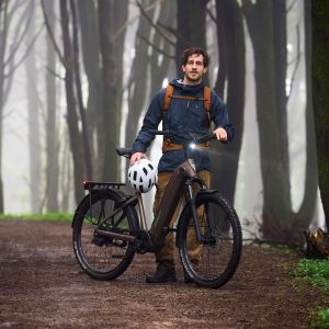 A cyclist stands in the forest behind his Giant AnyTour X E+ adventure bike.