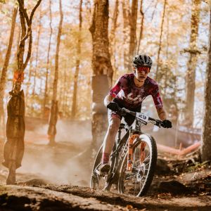 A mountain biker charges over a small tech feature on a xc race course riding her Liv Pique Advanced SL.