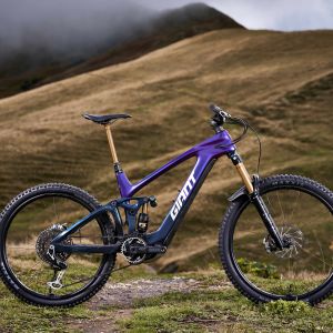 The Giant Reign Advanced E+ rests on a cloudy mountain trail with clouds in the background.