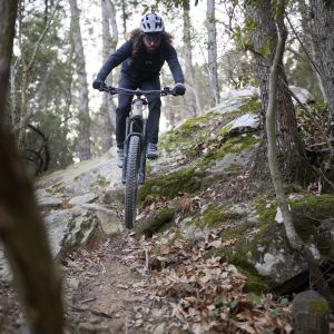  mountain biker riding a Giant Stance E+ trail bike rolls over a small hill into a flowing descent.