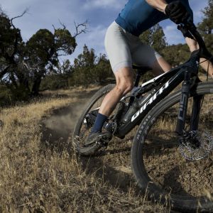 A mountain biker takes a bermed trail at speed riding their Giant Anthem Advanced SL cross country bike with Giant XCA wheels.