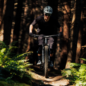 A mountain biker approaches on a wooded trail wearing Giant Shuttle Clip BOA shoes.