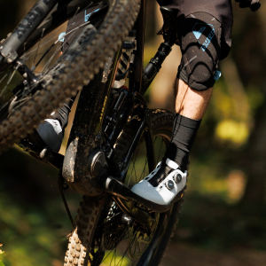 A mountain biker catches some air off a lip on a trail clipped into the pedals wearing Giant Shuttle Clip BOA shoes.