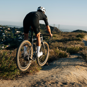 A gravel cyclist riding a titanium gravel bike with CADEX Max GXR wheels catches some air on a trail.