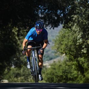 Cyclist rides out of the saddle on a Giant TCR Advanced under mature oak trees.