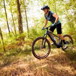 A female mountain biker rides a Liv Tempt E+ hardtail through the woods.