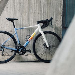 A Giant Contend SL aluminum road bike in the Birch Grey colorway leaning up against a wall in an urban environment. 