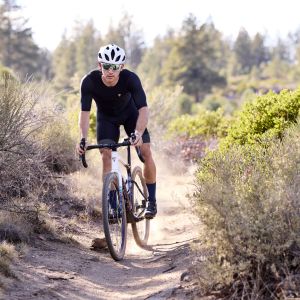 A gravel cyclist approaches on a forest trail riding their Giant Revolt Advanced SE.