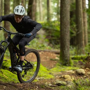 A mountain biker riding a Giant Stance skids through a chicane on a forested trail.