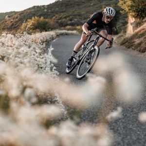 A road biker on a Giant Defy with Cadex Ultra 40 wheels leans into a corner on a descent.