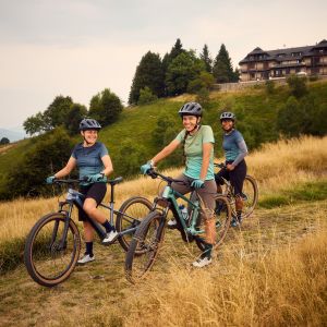 Three friends riding Liv Tempt E+ mountain bikes take a pause to chat on the side of a trail.