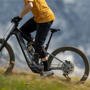 A mountain biker riding a Giant Trance Advanced E+ trail bike rides out of the saddle showing off the Contact Switch E+ dropper seatpost in the up position.