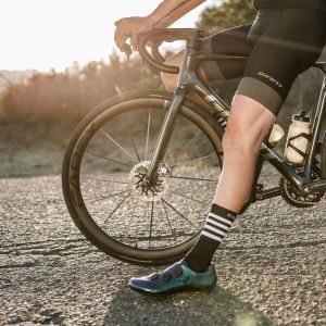 A road cyclist rests on their Giant Defy road bike with Cadex Ultra 40 wheels as the sun sets in the mountains behind.
