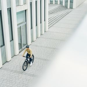 A commuting cyclist rides through the shadow of a large building on their Giant Talon E+ EX hardtail bike.