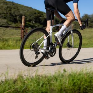 A rear view of a cyclist as they ride past wearing white Giant Surge road bike shoes.