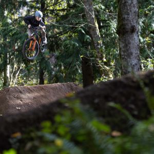 A young rider on a Giant STP 24 dirt jumper catches air off of a large dirt jump in the woods.