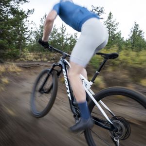 A cross country mountain biker on a Giant Anthem Advanced SL with a Giant Contact Switch SL dropper seatpost takes a corner at speed out of the saddle on a mountain trail.