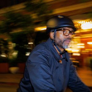 A cyclist rides through the city at night wearing a Giant Novo Mips helmet as he passes by lit up storefronts.