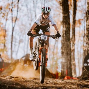 A mountain biker catches some air off a small jump in a xc race riding a Liv Pique Advanced SL CX bike.