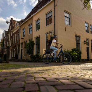 A woman rides around a cobbled street corner in a residential neighborhood on a Giant Entour E+ city bike.