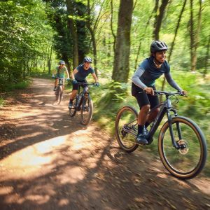 Three female mountain bikers on Liv Tempt E+ hardtail mtbs ride down a trail in the woods.