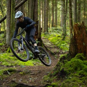 A trail mountain biker on a Giant Stance catches air off a tree stump.