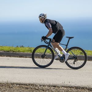 Road biker rides Giant TCR Advanced Pro 0 with ocean backdrop.