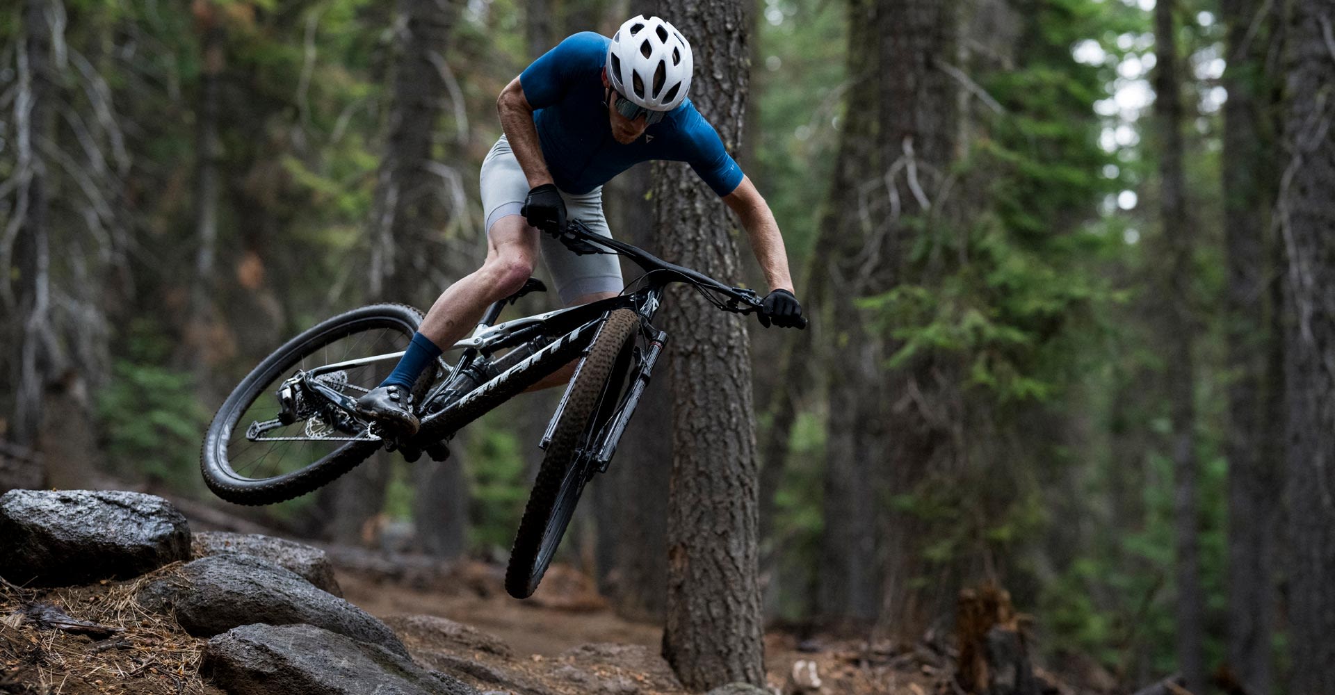 mountain biker riding over big rock in forest