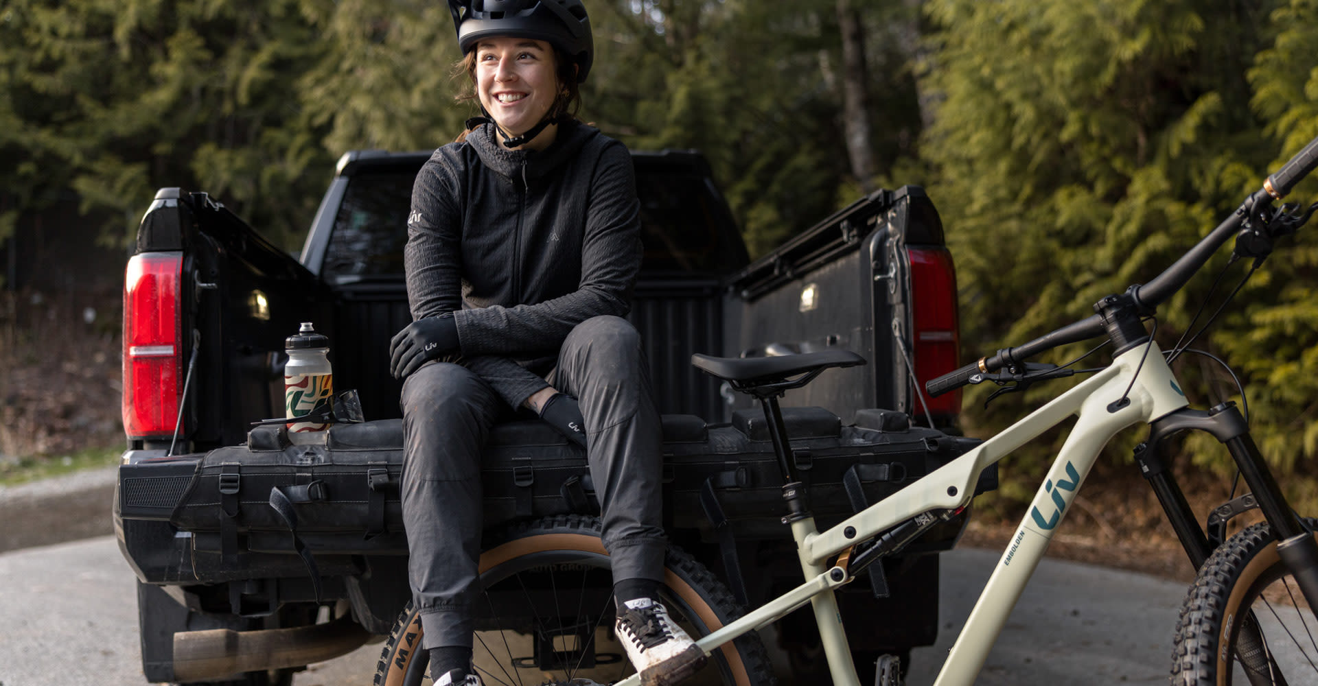 Woman sitting on bed of truck next to the Liv Embolden.