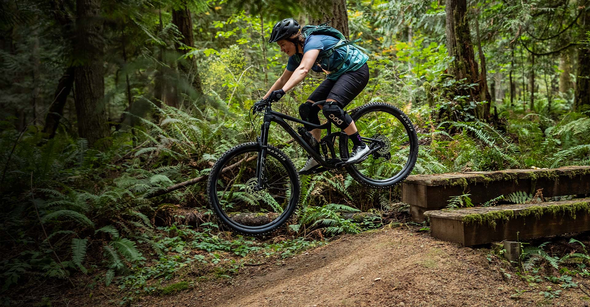 a woman riding a mountain bike off a wooden drop