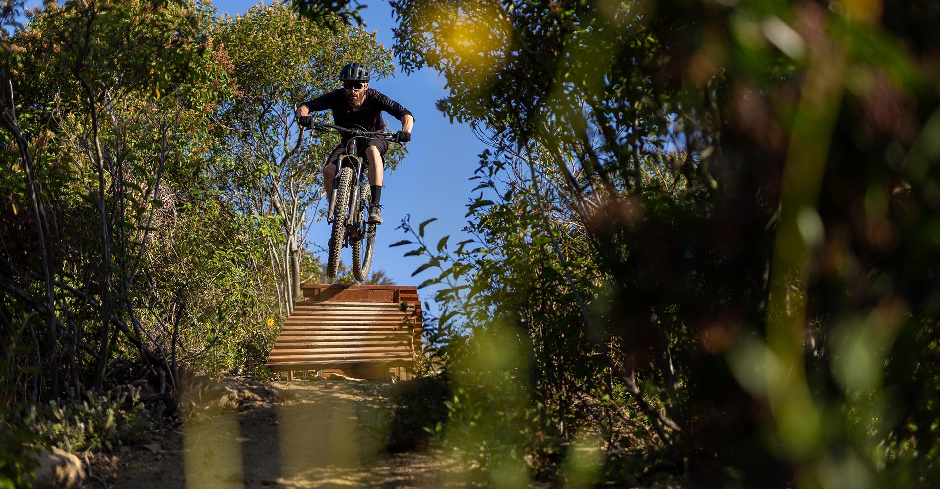 29 inch mountain bike rider descending from wooden ramp on mountain bike trail