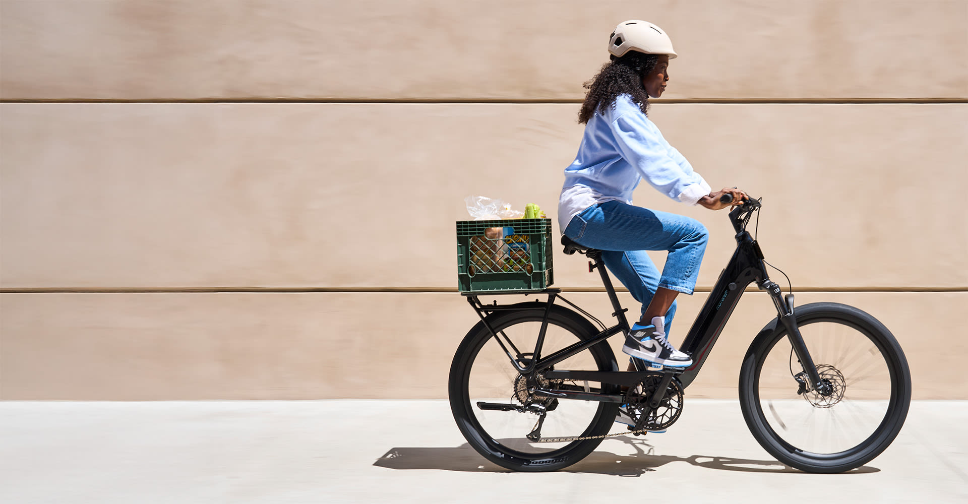 Woman riding the Momentum Vida E+ EX e-bike through a city street with cargo on the rear rack